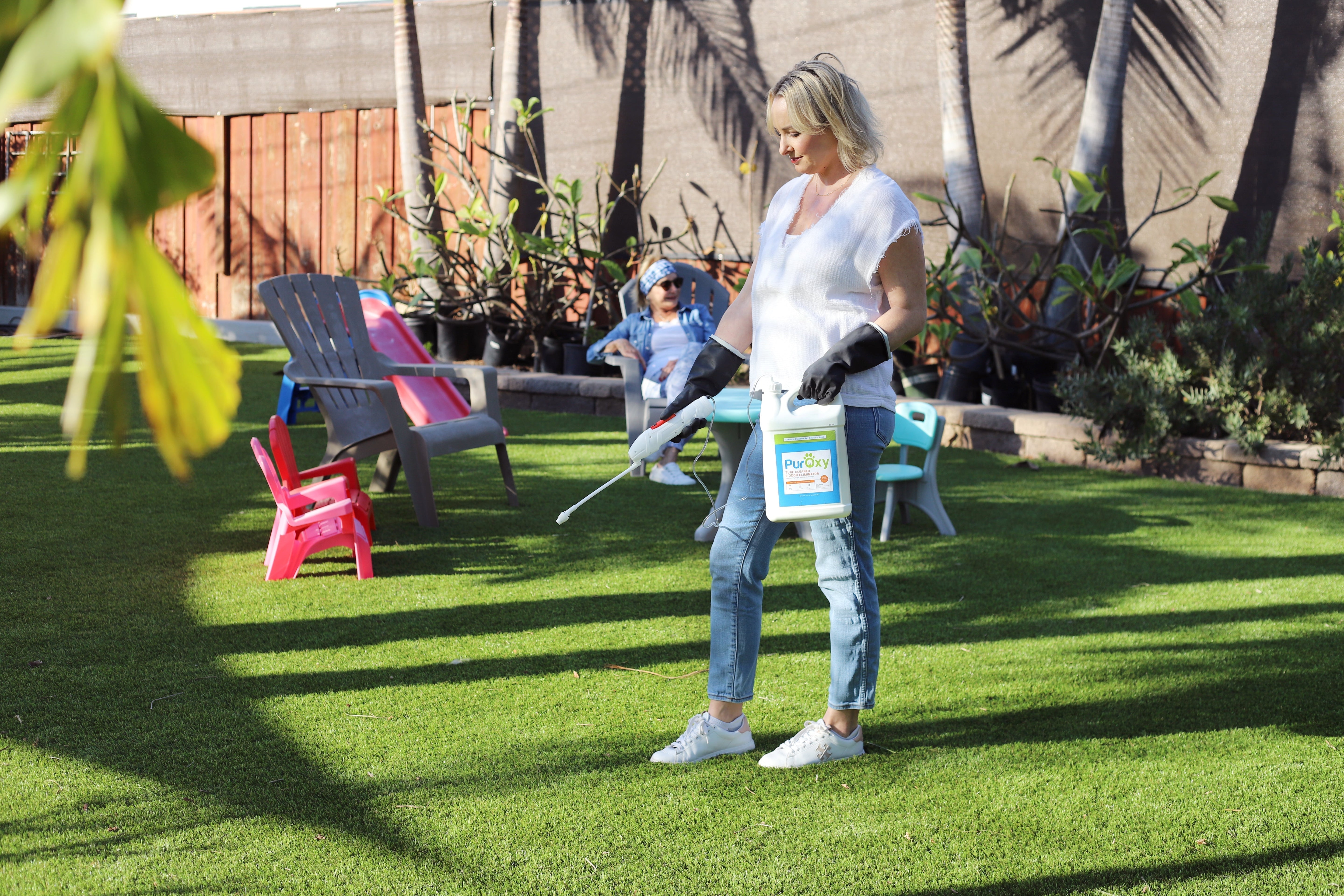 Woman spraying PurOxy outdoor pet stain cleaner on artificial turf